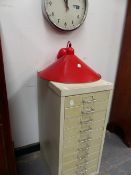 A SMALL FILING CABINET, A WALL CLOCK AND A CEILING LIGHT.