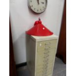 A SMALL FILING CABINET, A WALL CLOCK AND A CEILING LIGHT.