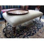 A LARGE REGENCY STYLE BANQUETTE STOOL WITH RING TURNED TAPERED LEGS ENDING IN BRASS CASTORS.