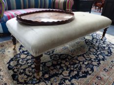A LARGE REGENCY STYLE BANQUETTE STOOL WITH RING TURNED TAPERED LEGS ENDING IN BRASS CASTORS.
