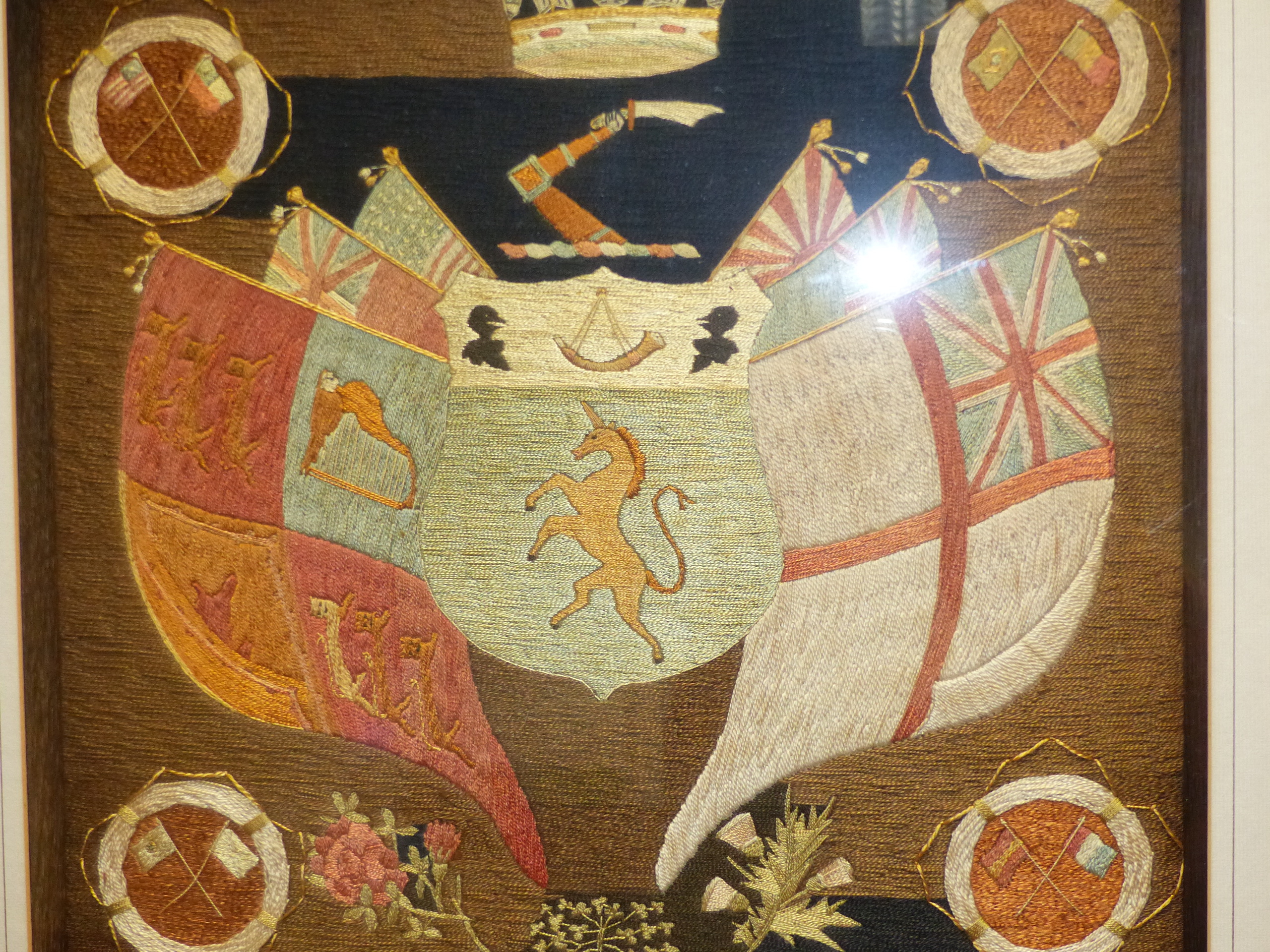 AN ANTIQUE SILKWORK PANEL OF AN ARMORIAL CREST SURROUNDED BY FLAGS IN BESPOKE SHADOW BOX FRAME. 42 x