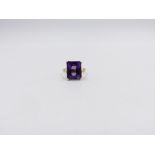 AN 18ct STAMPED YELLOW GOLD PURPLE SAPPHIRE DRESS RING. THE CENTRAL PURPLE SAPPHIRE IS AN EMERALD