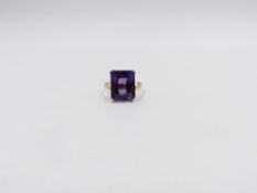 AN 18ct STAMPED YELLOW GOLD PURPLE SAPPHIRE DRESS RING. THE CENTRAL PURPLE SAPPHIRE IS AN EMERALD