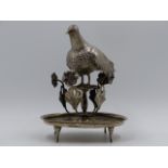A WHITE METAL SPANISH COLONIAL ORNAMENTAL FIGURE OF A BIRD WITH A HINGED TOP AND SUPPORTED ON AN