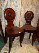 A PAIR OF REGENCY CARVED MAHOGANY SABRE LEG HALL CHAIRS, CIRCULAR BACKS WITH PAINTED ARMORIAL