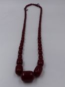 A GRADUATED CYLINDRICAL ROW OF CHERRY AMBER BEADS, APPROXIMATE LENGTH 92cms, APPROXIMATE