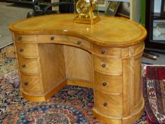 A MID VICTORIAN SATINBIRCH KIDNEY FORM DESK WITH INSET TOOLED LEATHER TOP ABOVE THREE APRON DRAWERS,