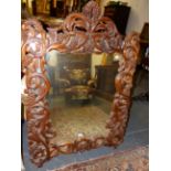 AN ELABORATELY CARVED FRAME MIRROR WITH SCROLLED PIERCED BRANCH FORM DECORATION WITH CLUSTERS OF