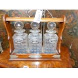 A LATE VICTORIAN OAK THREE BOTTLE LOCKING TANTALUS TOGETHER WITH THREE HALLMARKED SILVER SPIRIT