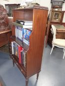 A MAHOGANY REGENCY STYLE WATERFALL BOOKCASE WITH BASE DRAWER ON REEDED TAPERED LEGS. H.121 x D.