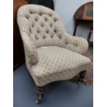 A VICTORIAN UPHOLSTERED BUTTON BACK ARMCHAIR ON RING TURNED FRONT LEGS ENDING IN CERAMIC CASTORS.