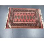 AN ORIENTAL RUG OF BOKHARA DESIGN AND THREE SMALL TRIBAL MATS.