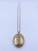 A 9ct HALLMARKED YELLOW GOLD LARGE OVAL SCROLL ENGRAVED LOCKET SUSPENDED ON A 9ct BELCHER CHAIN.