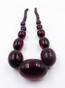 A GRADUATED ROW OF OVAL CHERRY RED AMBER BEADS. APPROXIMATE WEIGHT 87grms, APPROXIMATE LENGTH 54cms.