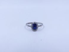 AN OVAL CUT SAPPHIRE AND DIAMOND HALO SET PLATINUM RING COMPLETE WITH DIAMOND SET SHOULDERS.