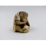 A SIGNED JAPANESE CARVED IVORY NETSUKE IN THE FORM OF A SEATED MONKEY OBSERVING AN INSECT ON A PIECE