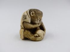 A SIGNED JAPANESE CARVED IVORY NETSUKE IN THE FORM OF A SEATED MONKEY OBSERVING AN INSECT ON A PIECE