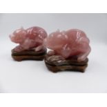 A PAIR OF CHINESE CARVED ROSE QUARTZ FIGURES OF CROUCHING MYTHICAL BEASTS ON HARDWOOD STANDS.