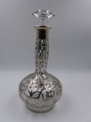 AN ART NOUVEAU GLASS DECANTER WITH OVERLAID WHITE METAL DECORATION. APPROXIMATE HEIGHT 28cms.