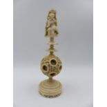A CARVED CANTONESE IVORY PUZZLE BALL ON STAND, THE FINIAL IN THE FORM OF A SEATED FIGURE WITH