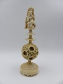 A CARVED CANTONESE IVORY PUZZLE BALL ON STAND, THE FINIAL IN THE FORM OF A SEATED FIGURE WITH