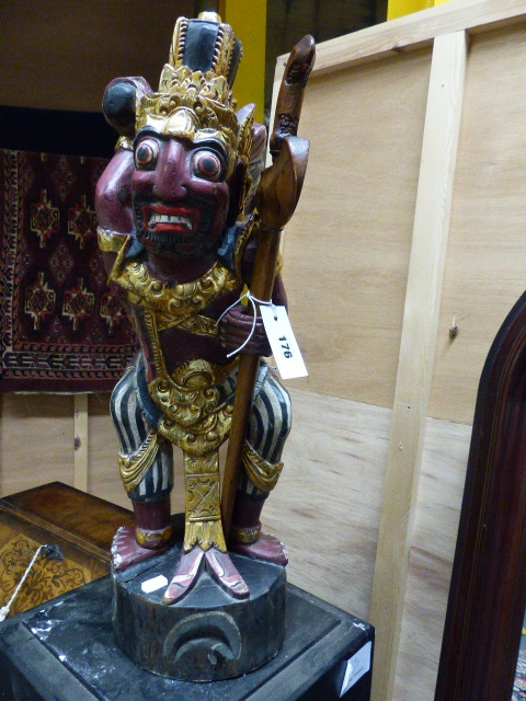 A CARVED AND DECORATED INDONESIAN FIGURE OF A MYTHICAL WARRIOR HOLDING A SWORD. H.61cms.