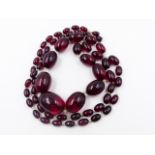 A GRADUATED ROW OF OVAL CHERRY AMBER BEADS. APPROXIMATE WEIGHT 113grms.