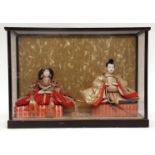 Two Japanese dolls representing the Emperor and the Empress seated on silk cushions and dressed in