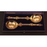Cased pair of silver gilt figural serving spoons, each with oval bowls to cast handles with winged