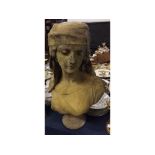 Composition sandstone coloured bust of a young lady with a head-dress, raised on a circular stand,