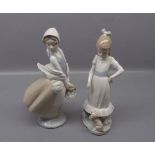 Two Nao models, one of hooded lady with basket of fruit and the other a young girl training her