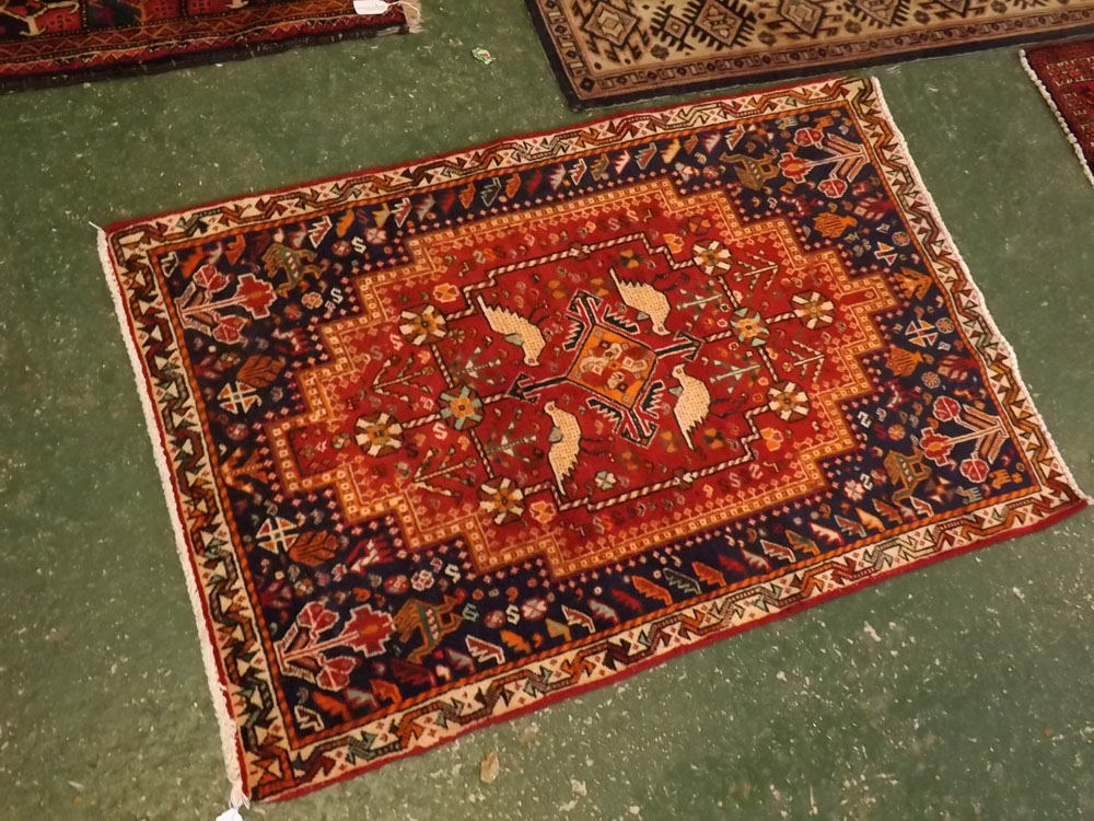 Modern wool carpet with geometric border and blue field with central red lozenge with bird and