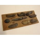 Display board of ten carved stone items including two with faces, board size 14ins x 6ins
