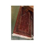 Small Bokhara style floor rug with rust ground, repeating geometric lozenge to centre, 33ins x 68ins