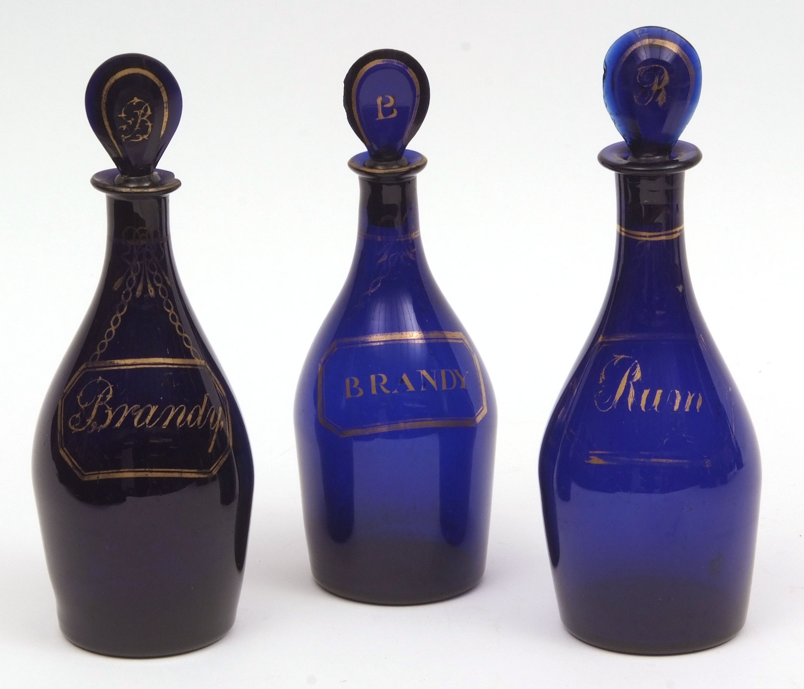 Three Bristol blue glass decanters, each with pear-shaped stoppers, comprising one for rum and two