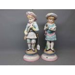 Pair of German bisque painted figures of a young boy holding a gun and a young girl with a doll,