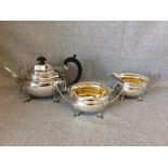 An oval silver three piece tea service, the teapot with ebony scroll handle, shell capped spout on