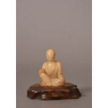 C17th Chinese soapstone figure of a Luohan, shown seated and holding a scroll above his raised right