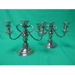 A pair of silver on copper three light candlesticks on circular loaded base. 18cm high