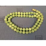 Jade bead necklace, the sixty three beads of approx. 1 - 1.2cm diameter, to a clasp stamped '585',