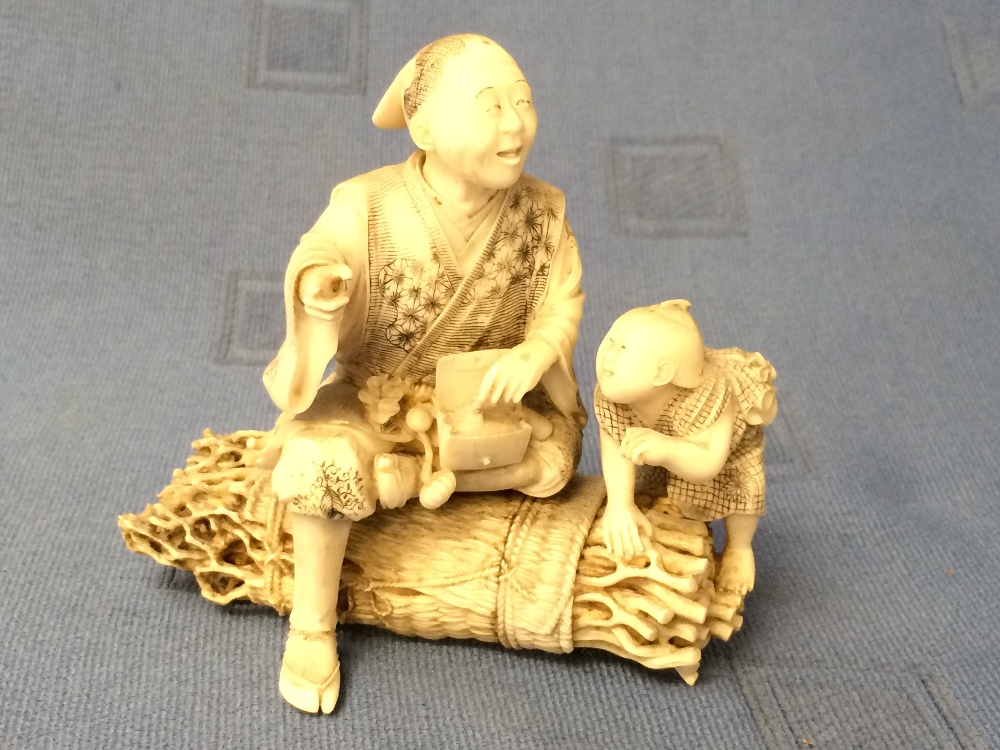 C19th intricately carved ivory Chinese figure group of a man and child on a bundle of sticks, red