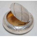 Circular silver trinket box [?] in the shape of a football with stitching and seams to ball.