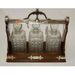 A 1920s oak three bottle tantalus having a silver plated mount and locking stile containing three