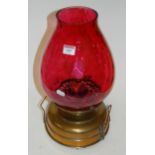 An early 20th century brass oil lamp having cranberry glass shade later converted to electricity,