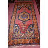 A Persian woollen red ground rug, having geometric floral stylised trailing tramline borders,