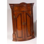 An early 19th century North Country oak and mahogany crossbanded bowfront hanging corner cupboard,