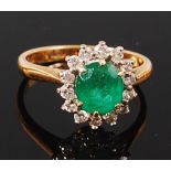 An 18ct gold, emerald and diamond cluster ring, the oval cut claw set emerald weighing approx 1ct,