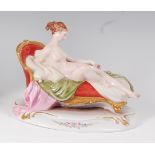 A Dresden porcelain figure of a reclining female nude upon a scroll-end settee,