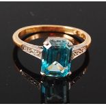 An 18ct gold and blue topaz set dress ring, the emerald cut four claw set topaz in a raised setting,