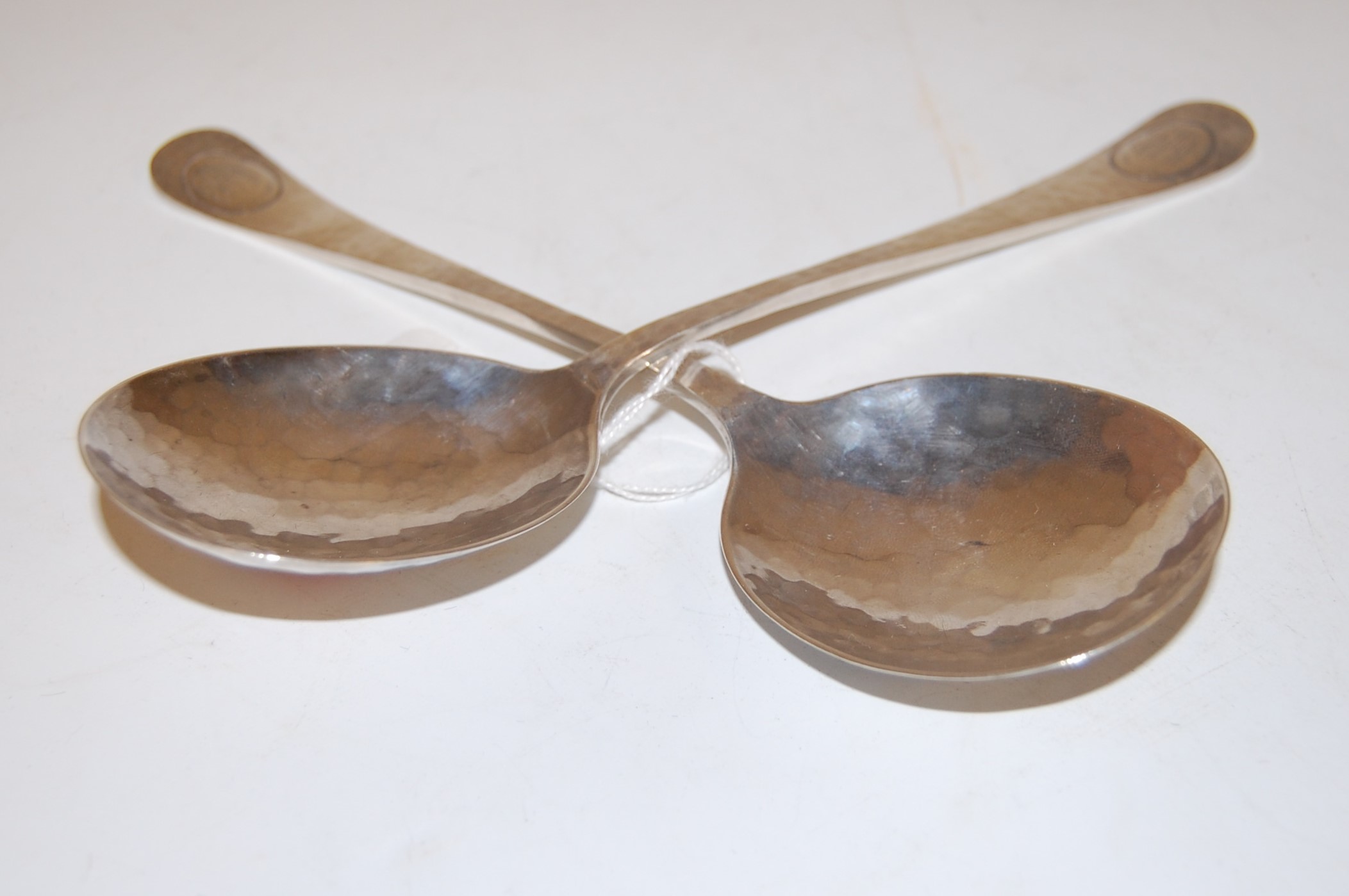 A pair of Arts & Crafts hammered silver spoons, each having a shallow bowl,